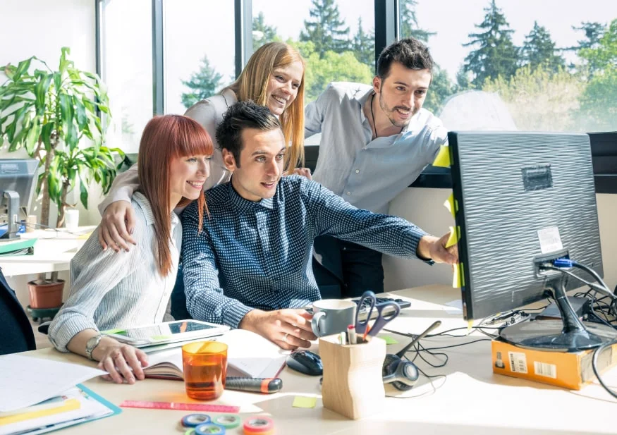 Team brainstorming session – male explaining web design project on PC screen to colleagues